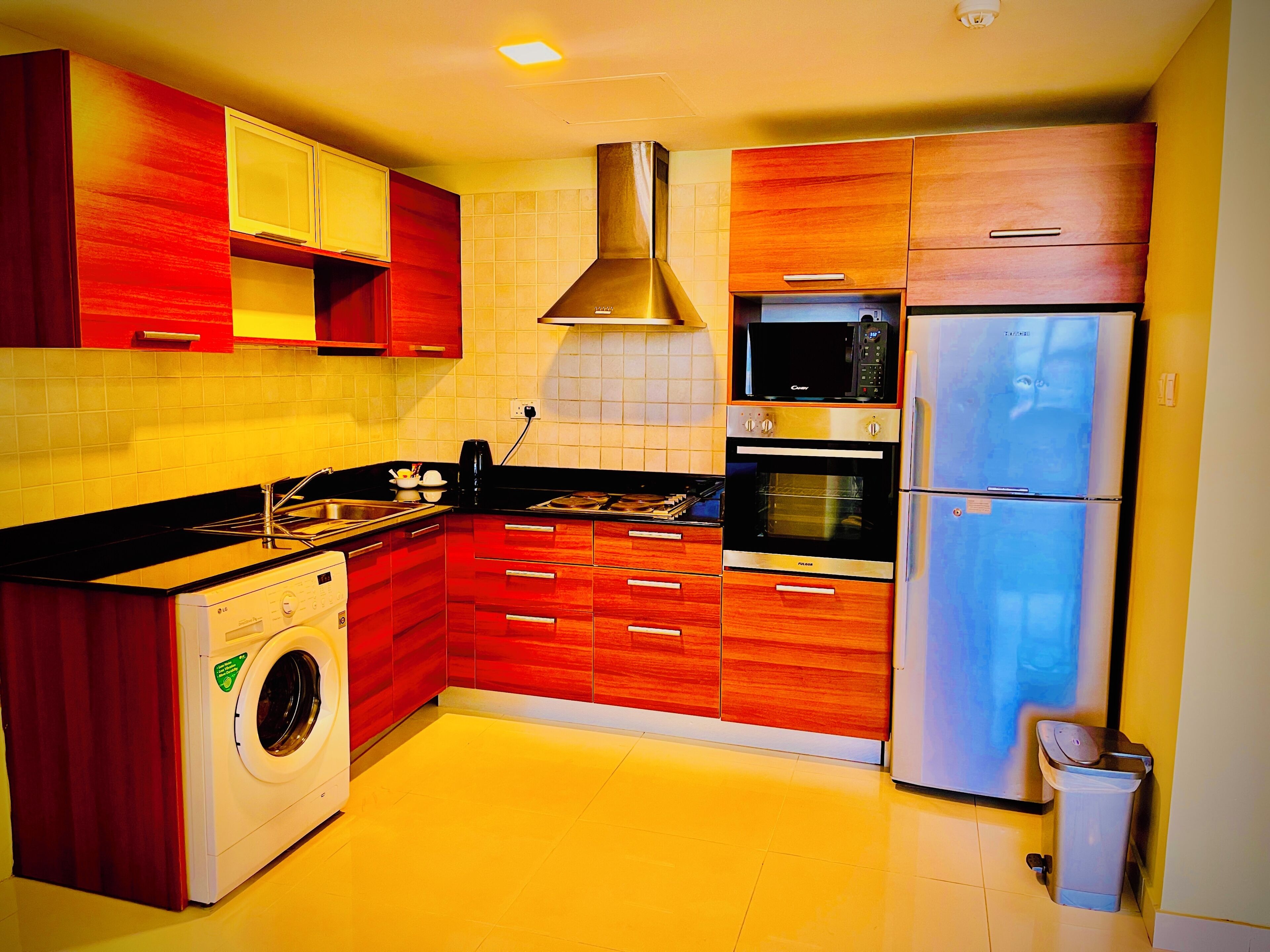 Una cucina compatta con mobili in legno, una lavatrice, un forno a microonde, un forno e un frigorifero.