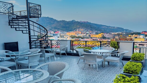 A rooftop terrace with wicker furniture, a spiral staircase, and a view of a colorful cityscape. - Hotel Wonder Hills @ Har ki Pauri Road Haridwar (Haridwar)