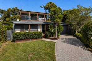 Une maison moderne à deux étages dotée d’un espace extérieur aménagé avec un coin salon couvert, d’une allée pavée et d’un jardin bien entretenu.
