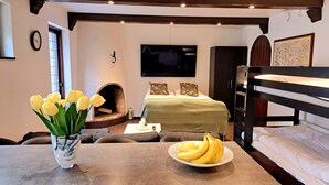 A cozy room with a bed, a TV, a fireplace, and a dining area with a plate of bananas and a vase of flowers. - TG Oasis Örgryte Stugor & Rum (Gothenburg)