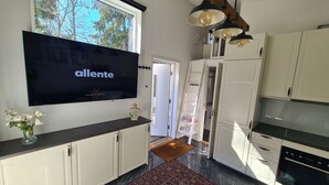 A modern kitchen with a flat-screen TV, white cabinets, a patterned rug, and a wooden ceiling beam. - TG Oasis Örgryte Stugor & Rum (Gothenburg)