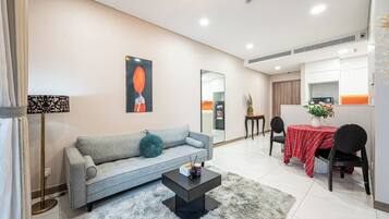 A modern living room with a grey sofa, a coffee table, and a dining area with a red tablecloth.