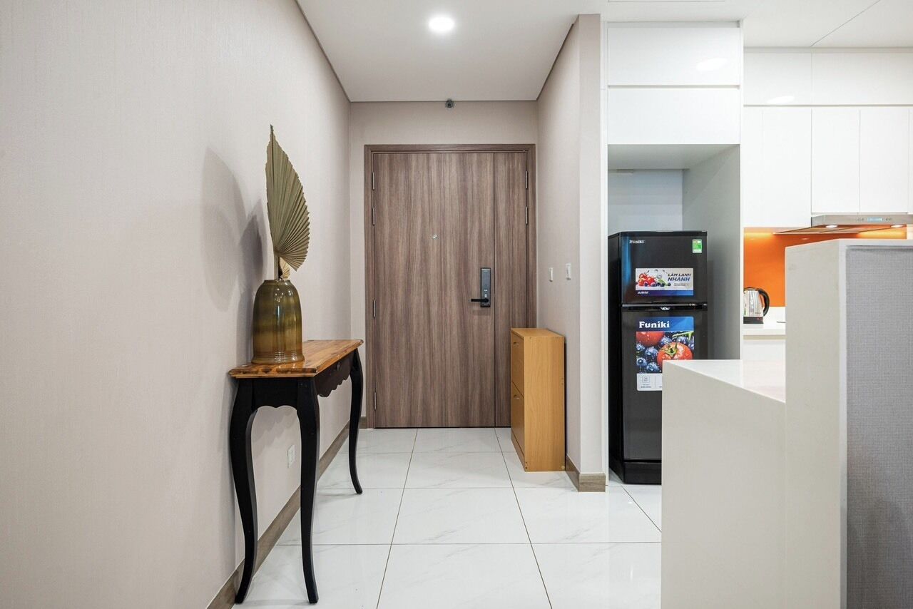 A hallway with a wooden door, a small table with a vase, and a refrigerator with a 'Funiki' label.