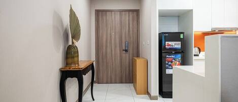 A hallway with a wooden door, a small table with a vase, and a refrigerator with a 'Funiki' label.