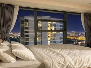 Habitación de hotel con una cama grande, vistas a un paisaje urbano nocturno y una ventana con cortinas.