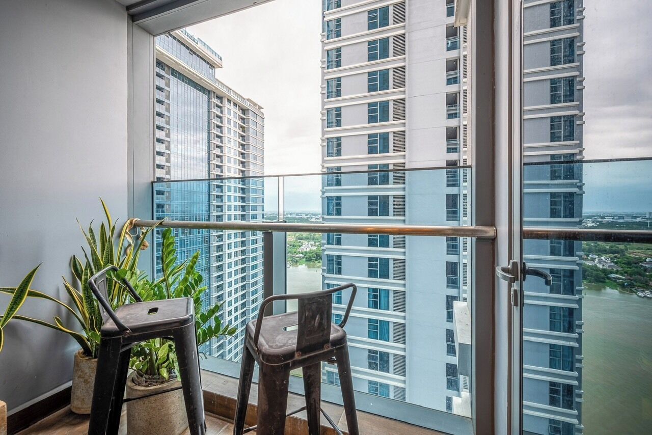 A balcony with two chairs and potted plants, overlooking a river and high-rise buildings.