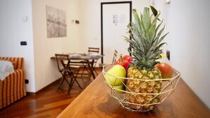 A dining area with a wooden table, chairs, and a fruit basket containing a pineapple, apple, and tomato. - HOUSE OF PRINCE AMBA ALAGI (ST. MARITIME) GENOVABNB.IT (GENOVA)