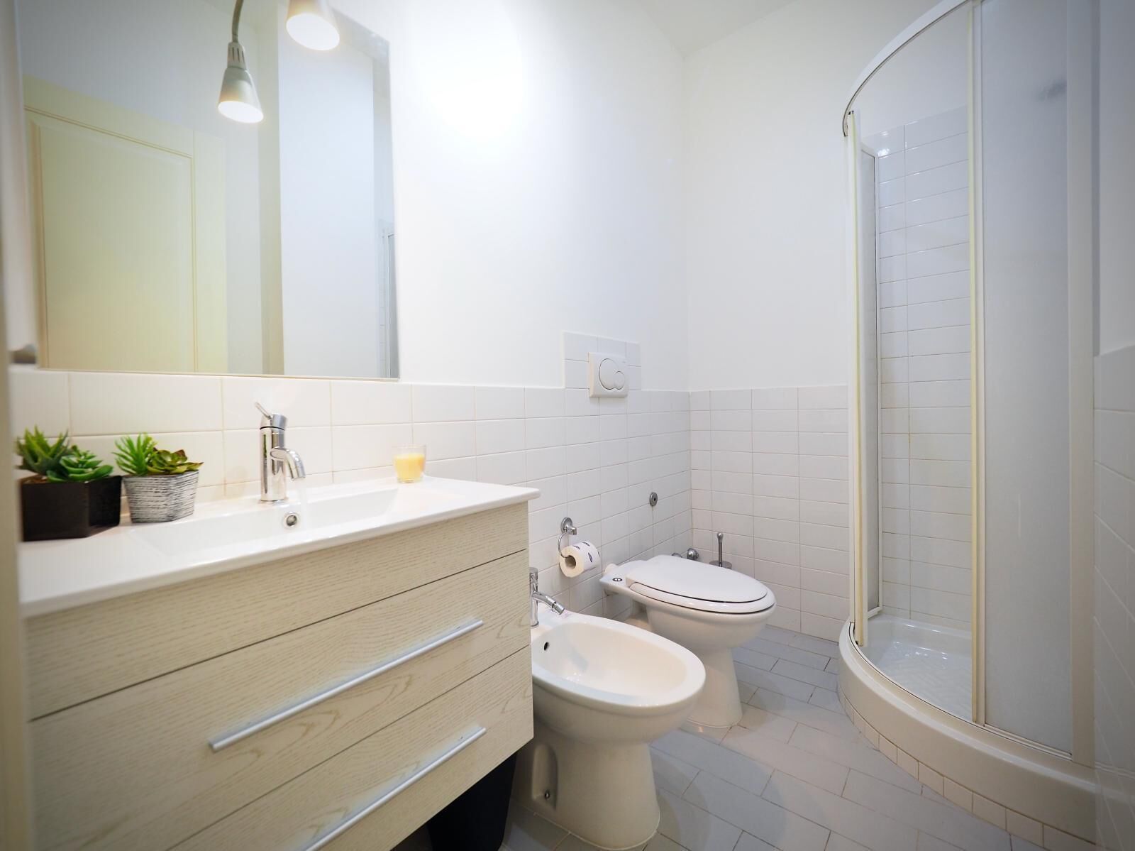 Une salle de bain moderne avec un meuble-lavabo blanc, un miroir, un évier, des toilettes et une douche à parois de verre.