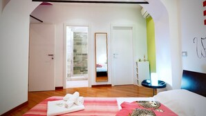 Een hotelkamer met een bed, een douche, een spiegel en een klein tafeltje met een lamp.