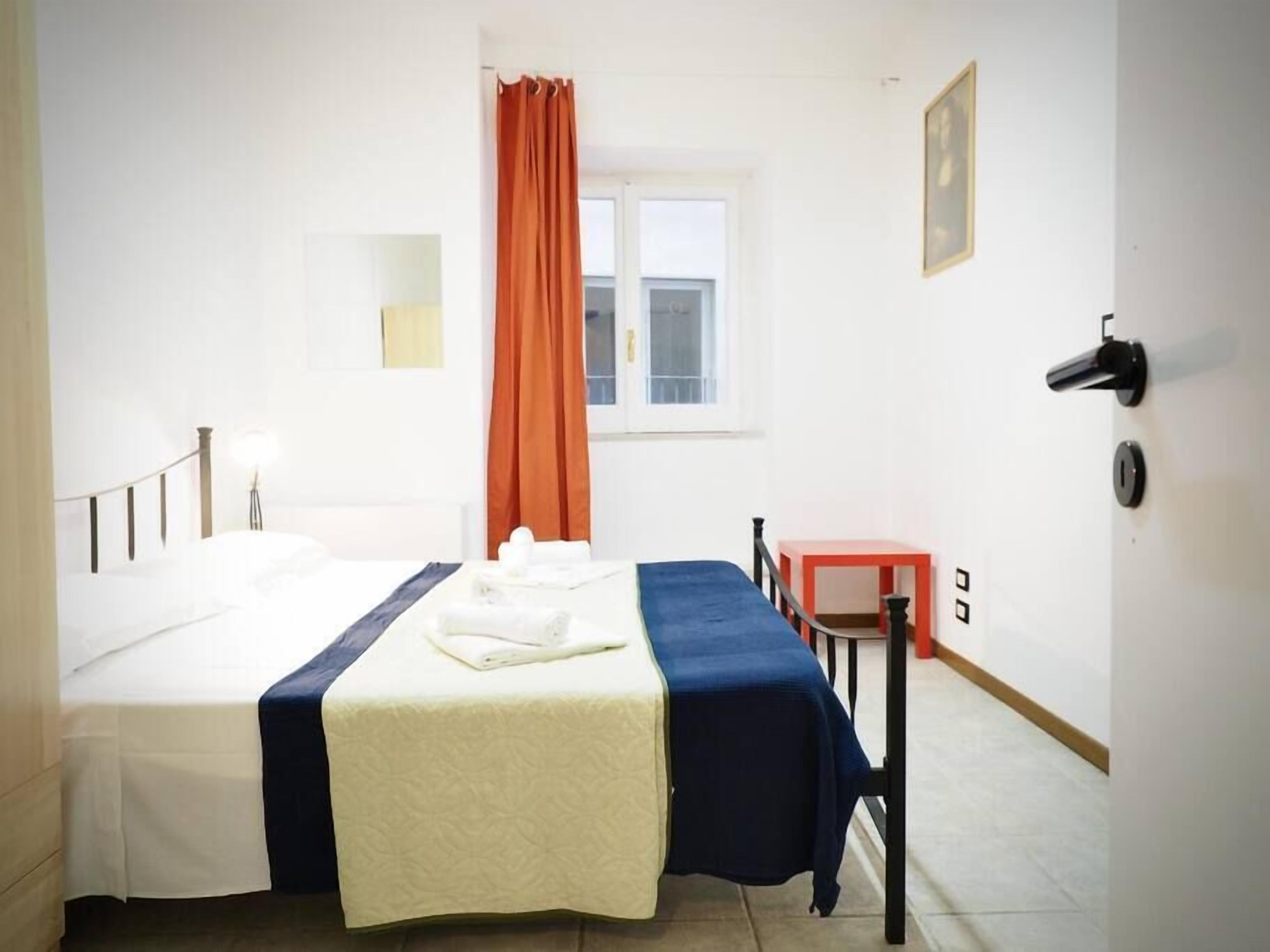 Ein Hotelzimmer mit einem Bett, einem Schreibtisch, einem Sessel, einem Fenster mit Vorhängen und einer Wandlampe.
