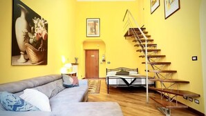 Een woonkamer met een bank, een bed, een trap en kunstwerken aan de wanden.
