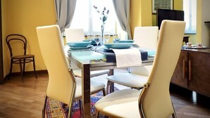 Een eetruimte met een tafel voor vier personen, stoelen, een bloemenvaas en een raam met gordijnen.
