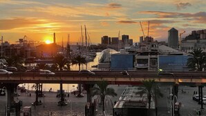 Un paisaje urbano con un atardecer, una marina con barcos y un puente sobre el agua.