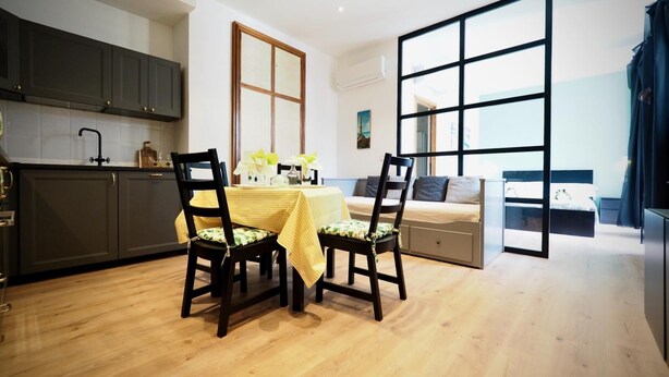 Una cocina moderna con armarios oscuros, una mesa de comedor con dos sillas y un ventanal grande.
