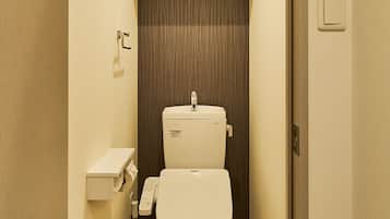 A compact bathroom with a toilet, a small shelf with a plant, and a wall-mounted telephone.