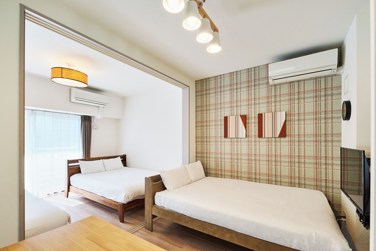 A hotel room with two beds, a wooden table, an air conditioning unit, and a television.