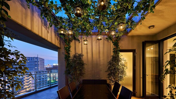 A balcony with a dining table and chairs, surrounded by plants and hanging lights. - ALFACIO RIVERSIDE STAY HAKATA (Fukuoka)