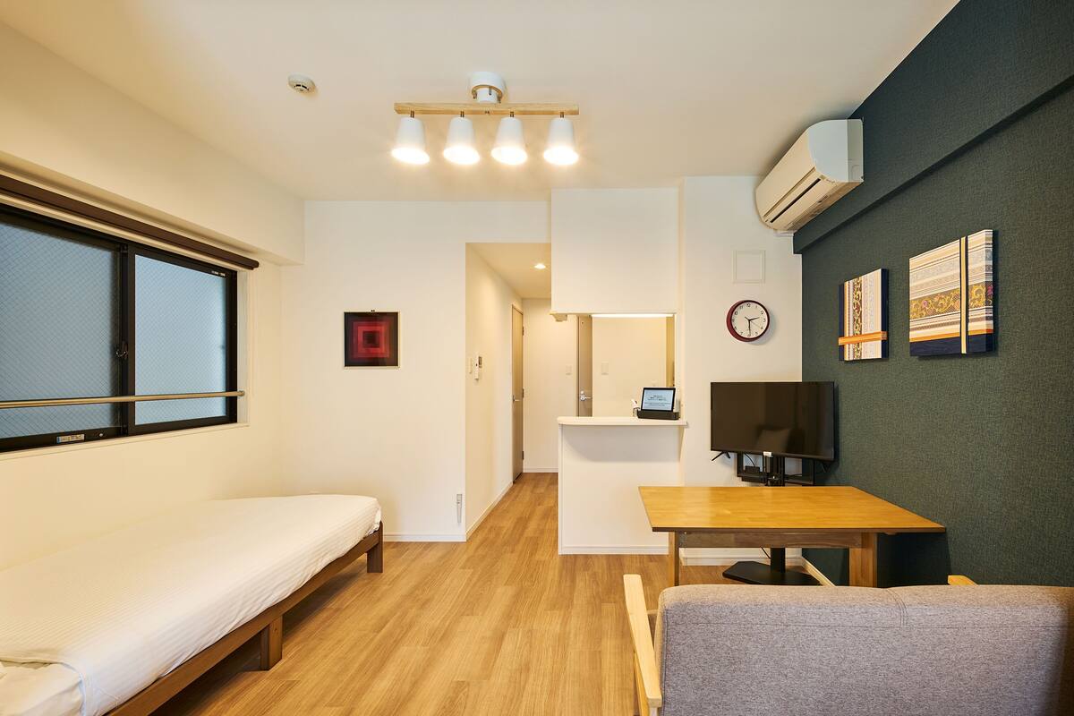 A compact room with a bed, a desk, a chair, a TV, and artwork on the wall.