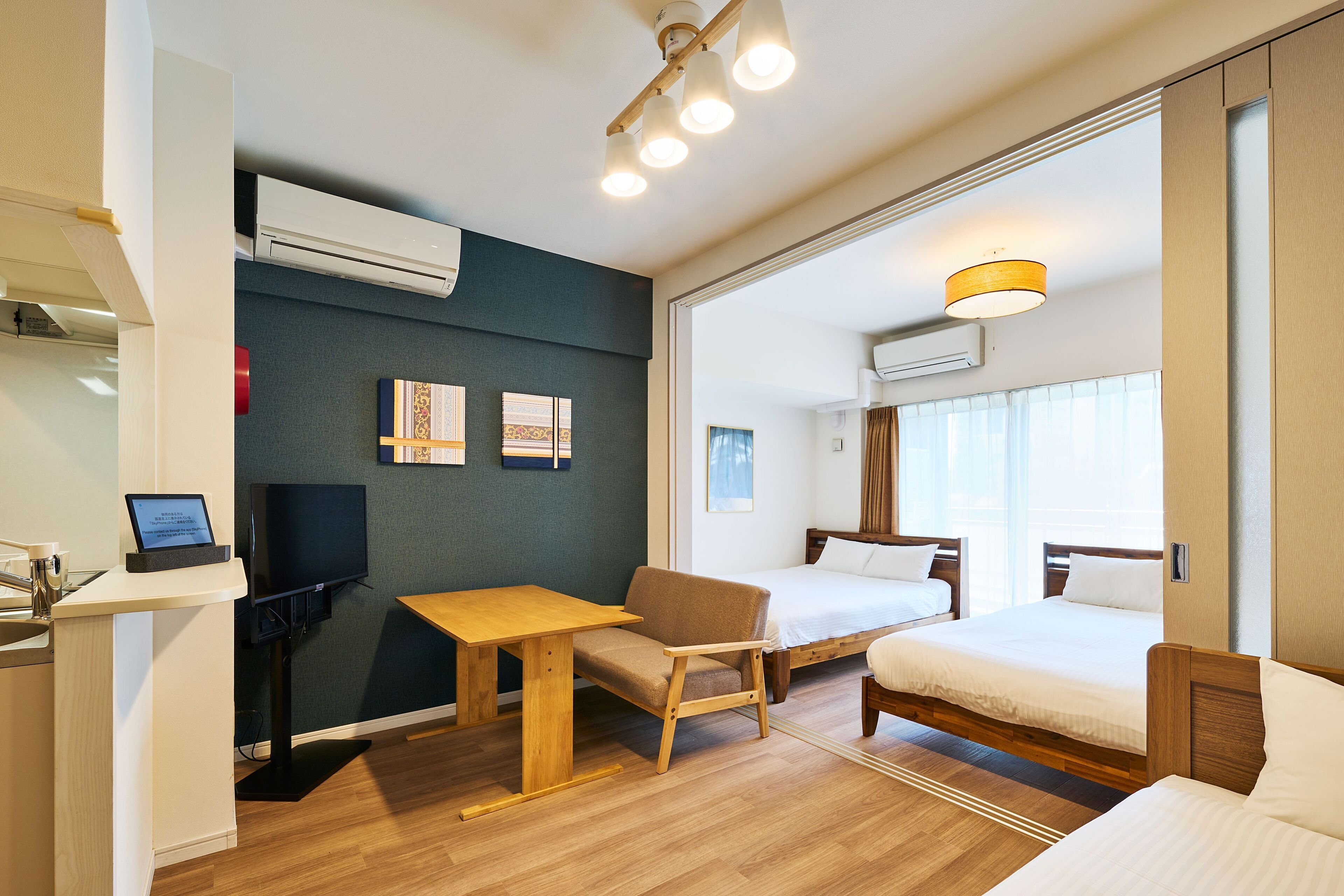 Une chambre d’hôtel avec un bureau en bois, deux lits simples, une télévision et des œuvres d’art accrochées au mur.
