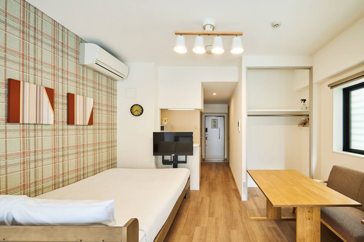 A modern hotel room with a bed, a TV, a wooden table, and a sofa.