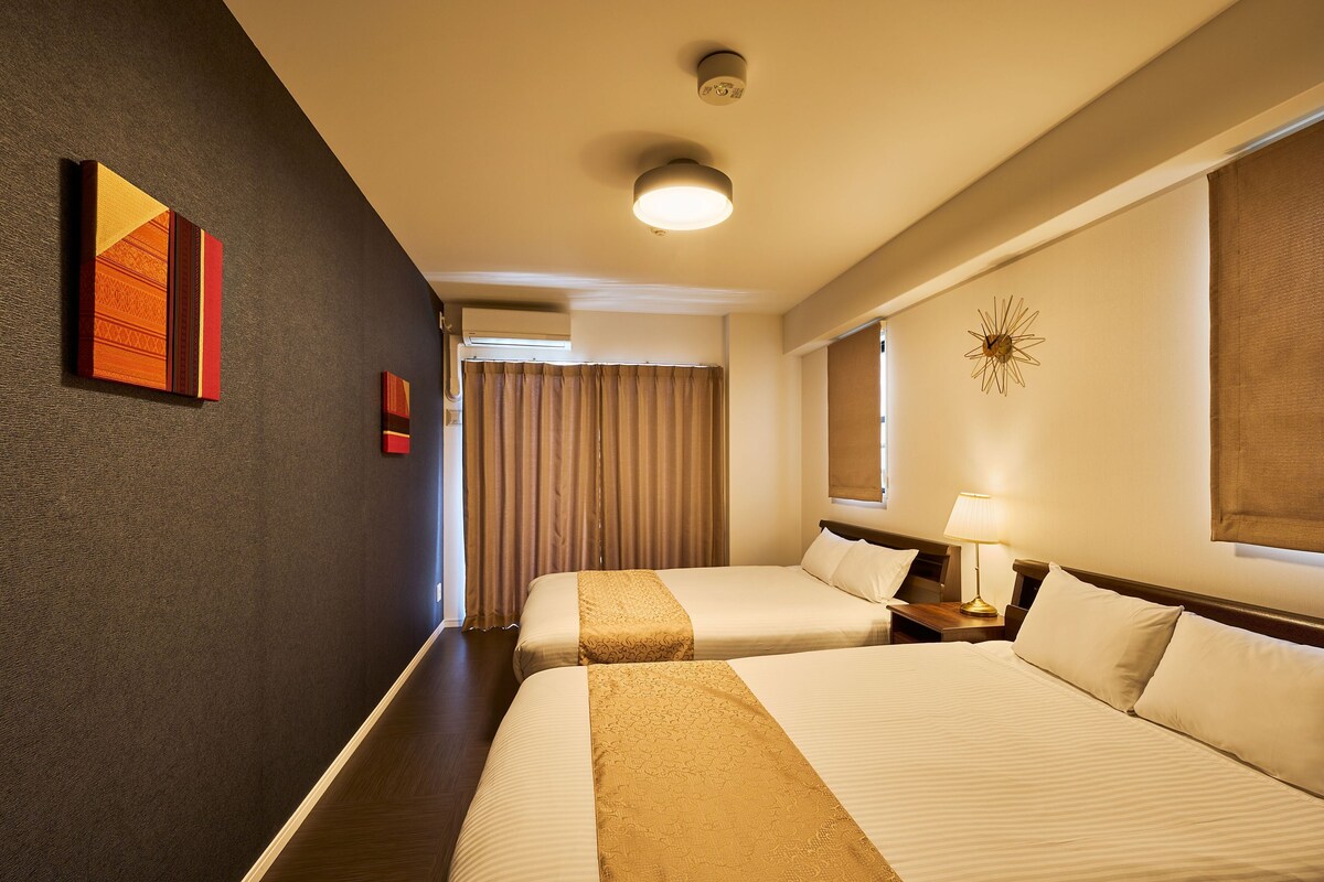 A hotel room with two beds, a nightstand with a lamp, a wall clock, and a window with curtains.