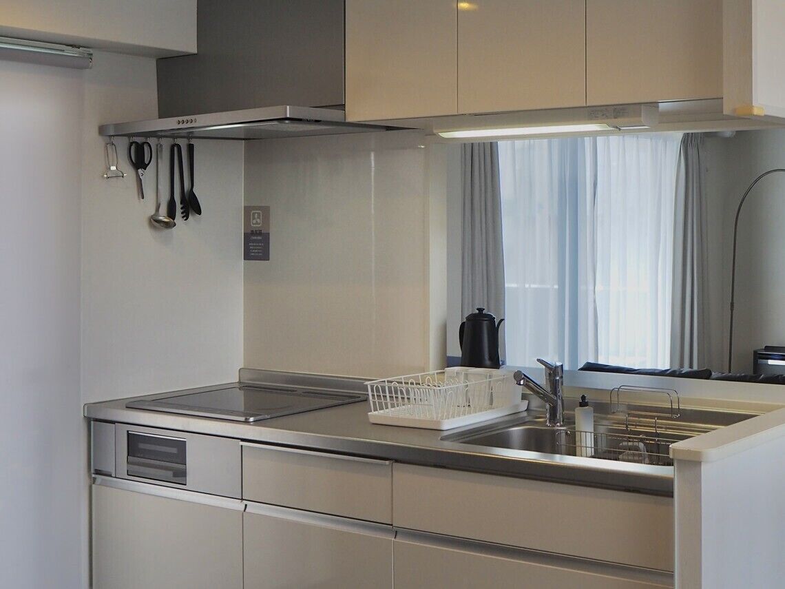 Una cocina moderna con electrodomésticos de acero inoxidable, horno integrado y una ventana con cortinas.