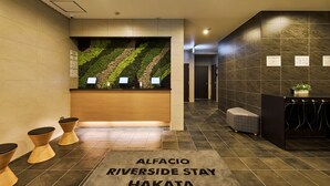 A reception area with a green wall, wooden reception desk, and a sign reading "ALFACIO RIVERSIDE STAY HAKATA". - ALFACIO RIVERSIDE STAY HAKATA (Fukuoka)