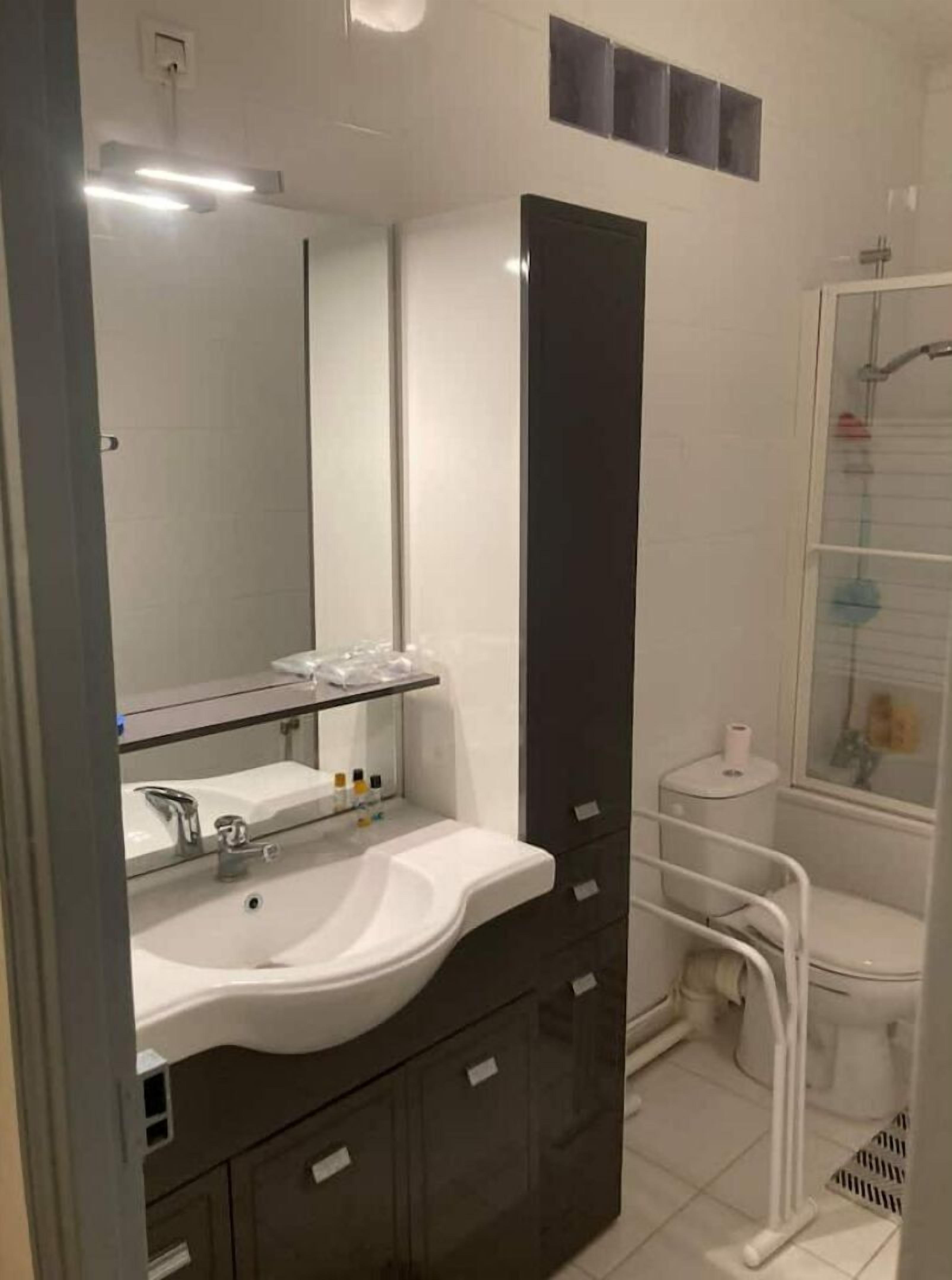 A modern bathroom with a large mirror, a white sink, dark cabinets, and a shower area.