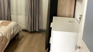 Ein kleines Hotelzimmer mit Bett, Schreibtisch und einem an der Wand befestigten Fernseher.
