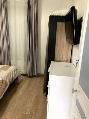 Pieni hotellihuone, jossa on sänky, pieni työpöytä ja seinälle asennettu televisio.