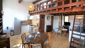 Cucina spaziosa con travi in legno, zona pranzo con tavolo rotondo e un soppalco accessibile tramite una scala.