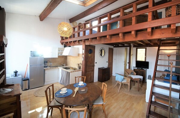 A spacious kitchen with wooden beams, a dining area with a round table, and a loft space with a ladder. - Rare Cassis duplex apartment, 5 minutes from the beach and port on foot (Cassis)
