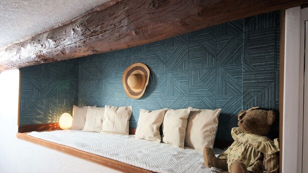 Una camera accogliente con travi a vista in legno, una parete decorata e un letto con copripiumino bianco, con un orsetto di peluche sopra.
