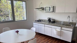 A modern kitchen with white cabinets, a granite countertop, a microwave, a coffee maker, and a sink. There is a dining table with chairs and a vase of flowers.