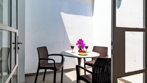 A small outdoor patio with a round table and four chairs, a vase of flowers, and two glasses of red wine.