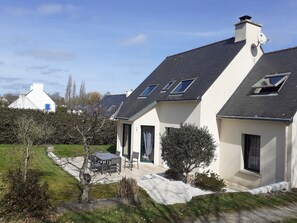 A modern house with a sloped roof, a patio with outdoor furniture, and a well-maintained garden.