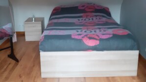 Ein Schlafzimmer mit schrägen Wänden, einem Bett mit floralem Überwurf, einem Nachttisch und einer Lampe.
