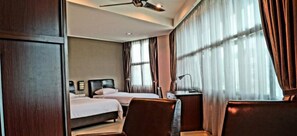 Hotellihuone, jossa on kaksi sänkyä, työpöytä, tuoli ja kattotuuletin.