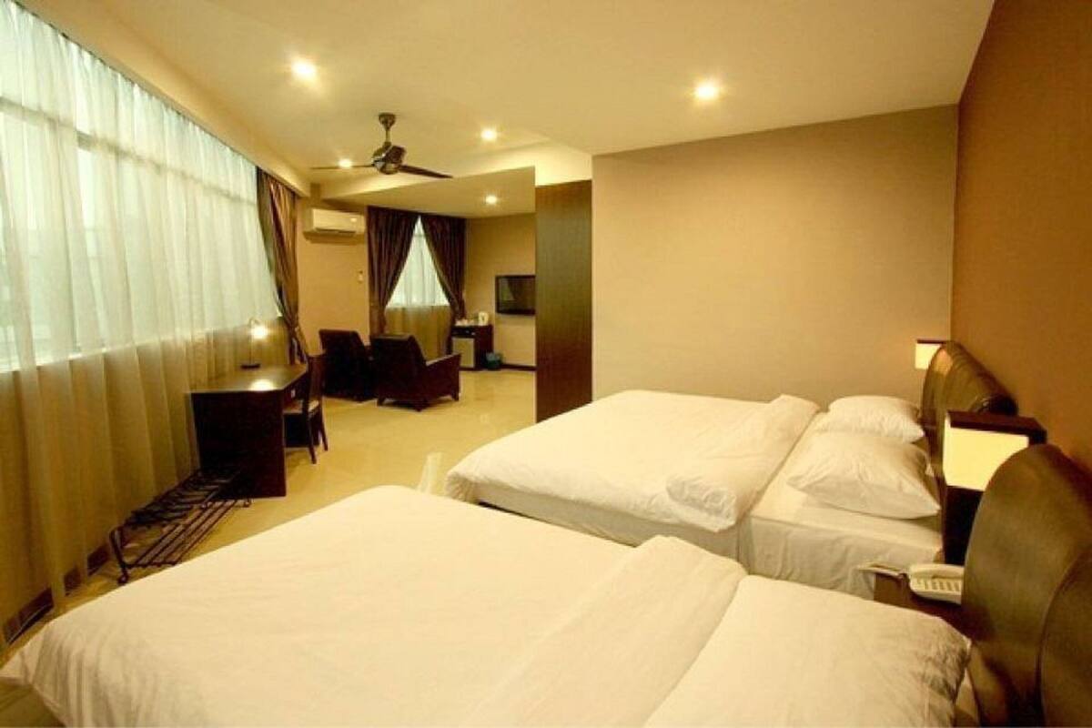 A hotel room with two beds, a desk, a chair, a TV, and a ceiling fan.