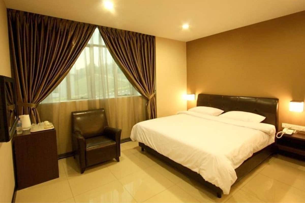 A hotel room with a bed, a chair, a nightstand, and a window with curtains.