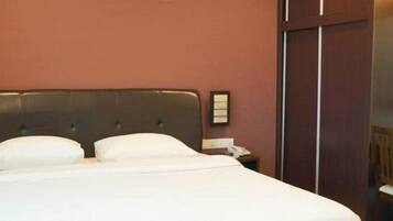 A hotel room with a large bed, a wooden nightstand, a desk, and a wardrobe.