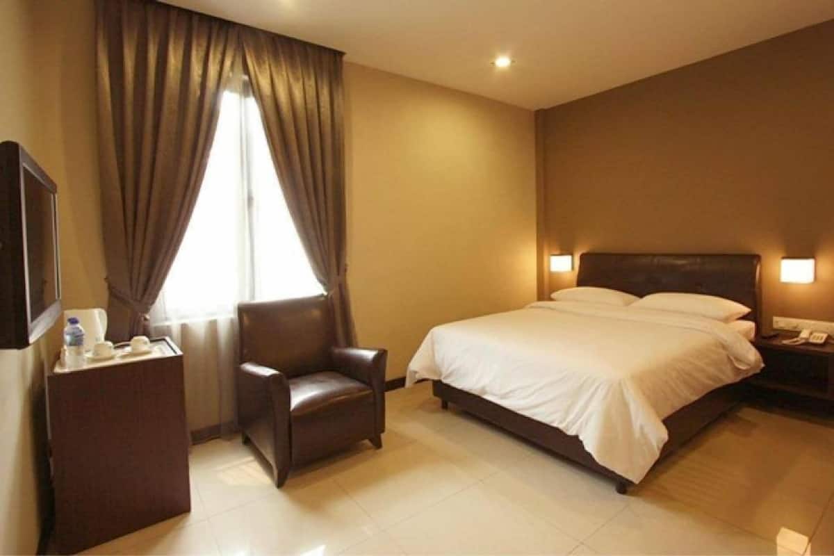 A hotel room with a bed, a chair, a bedside table, a lamp, and a window with curtains.