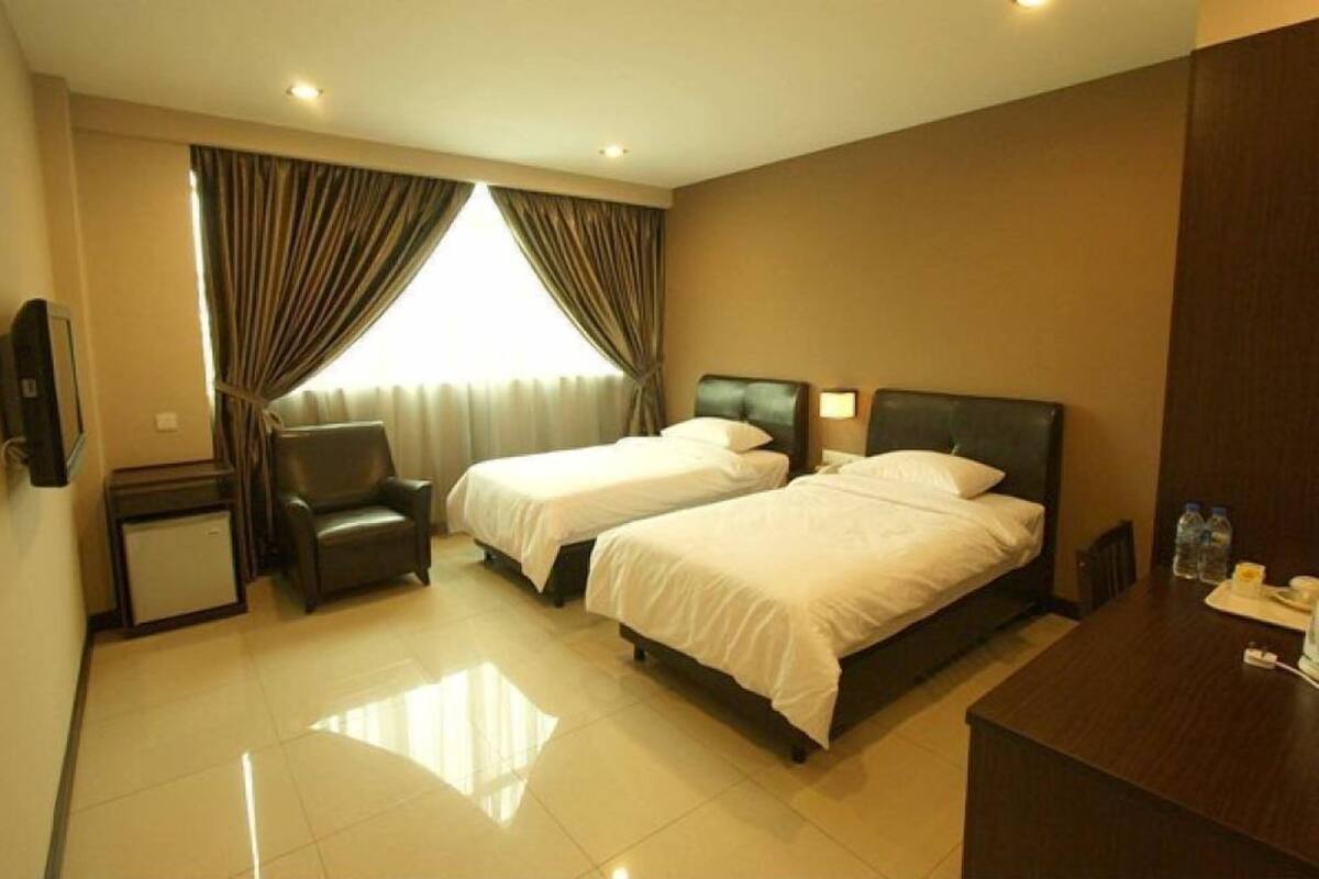 A hotel room with two beds, a desk, a chair, and a TV.