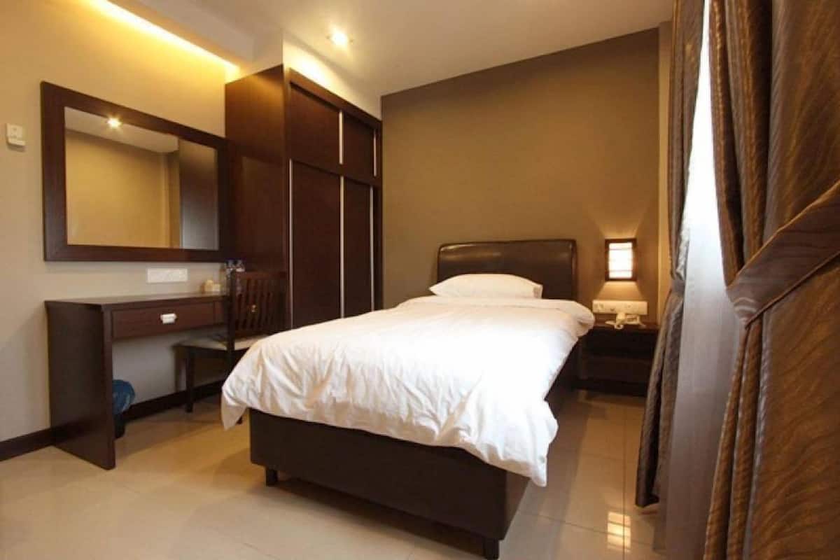 A bedroom with a large bed, a desk, a mirror, and a nightstand with a lamp.