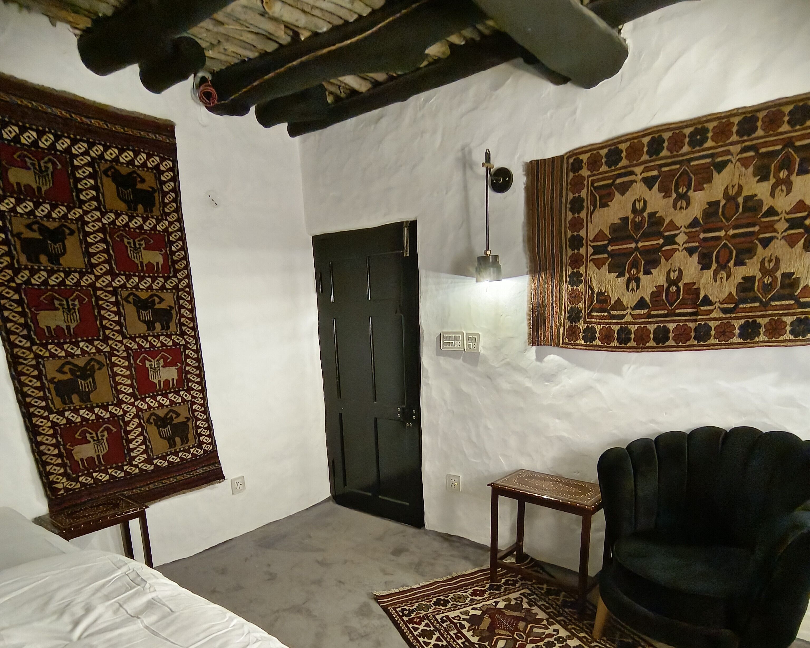 A room with a bed, a dark armchair, a door, and two large patterned rugs.