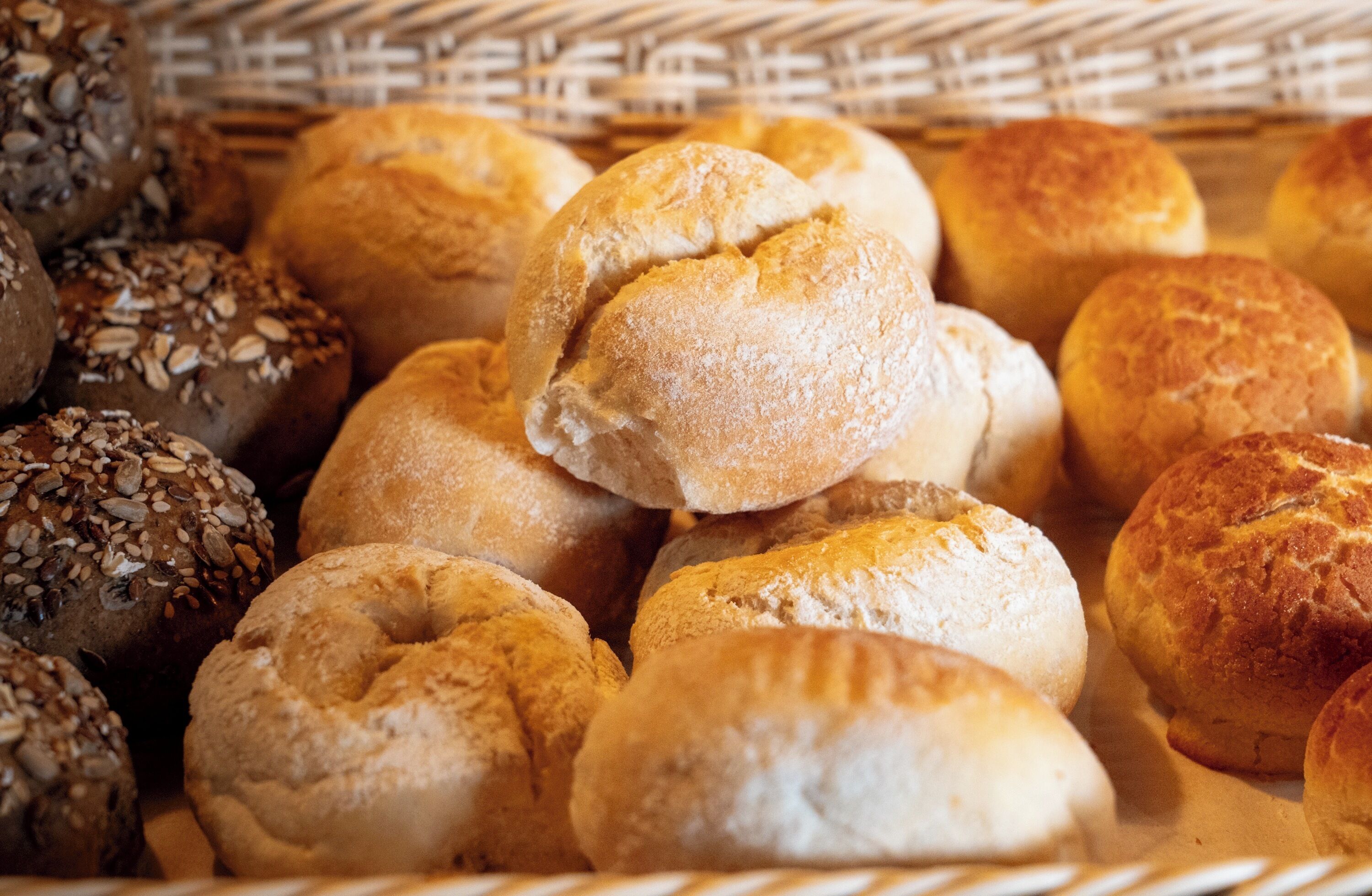 A basket filled with various types of bread, including some with seeds on top.