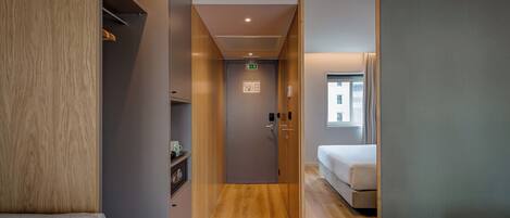 Quarto de hotel com piso de madeira, uma cama, guarda-roupa e espelho.