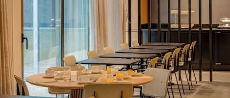 A dining area with round tables and chairs, breakfast items, and a view through large windows.