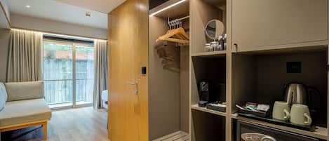 A hotel room with a sliding glass door to a balcony, a sofa, a wardrobe with hanging space, and a kitchenette area.