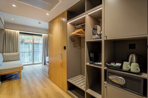 Habitación de hotel con puerta de vidrio corredera a un balcón, sofá, armario con espacio para colgar y una zona de kitchenette.